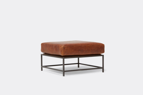 side of ottoman with brown leather upholstery on black metal frame