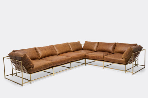 front of sectional with tan leather upholstery and brown leather belts on antique brass metal frame