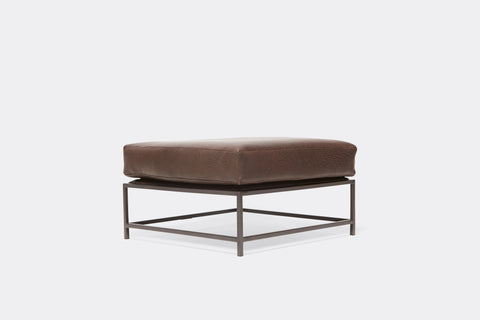 side of ottoman with brown leather upholstery on black metal frame